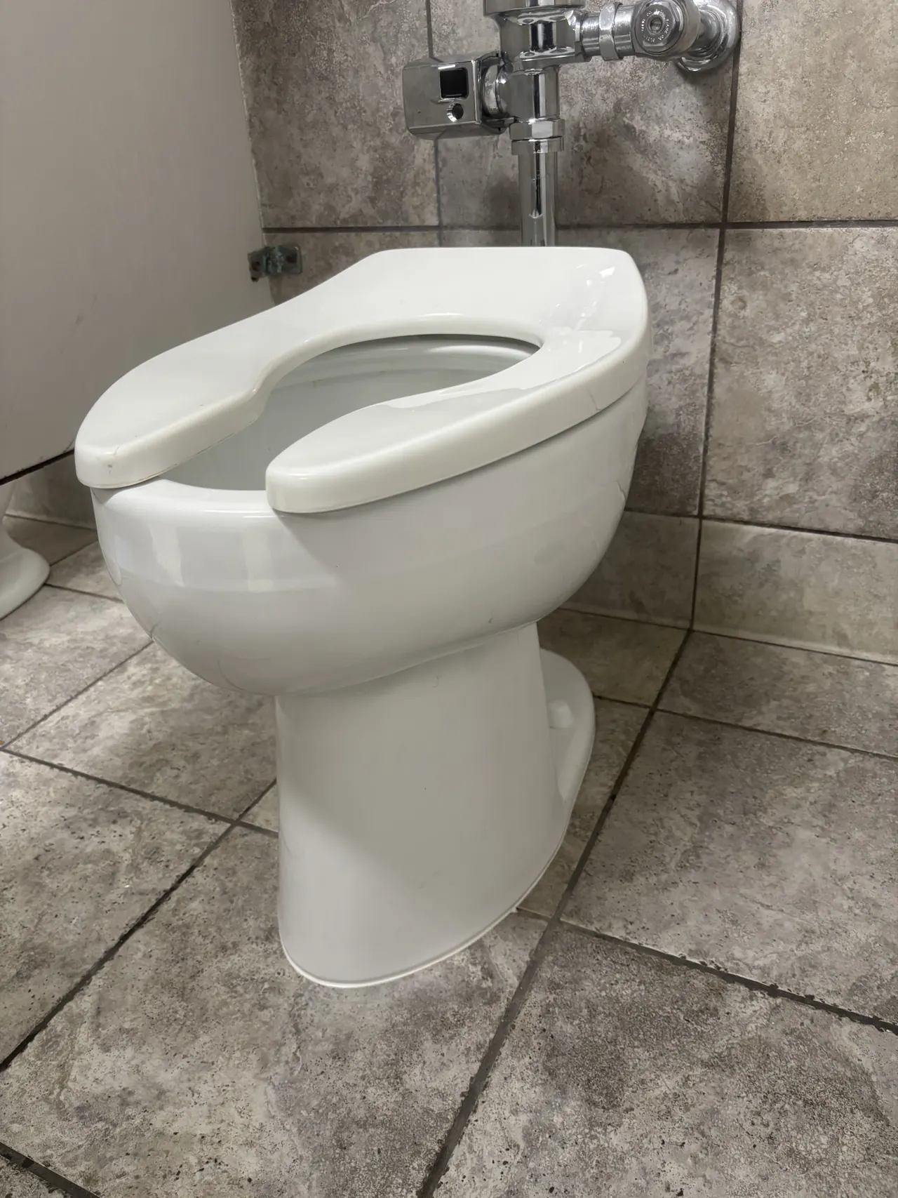 A commercial floor-mounted toilet with a sensor flush valve in a tiled restroom