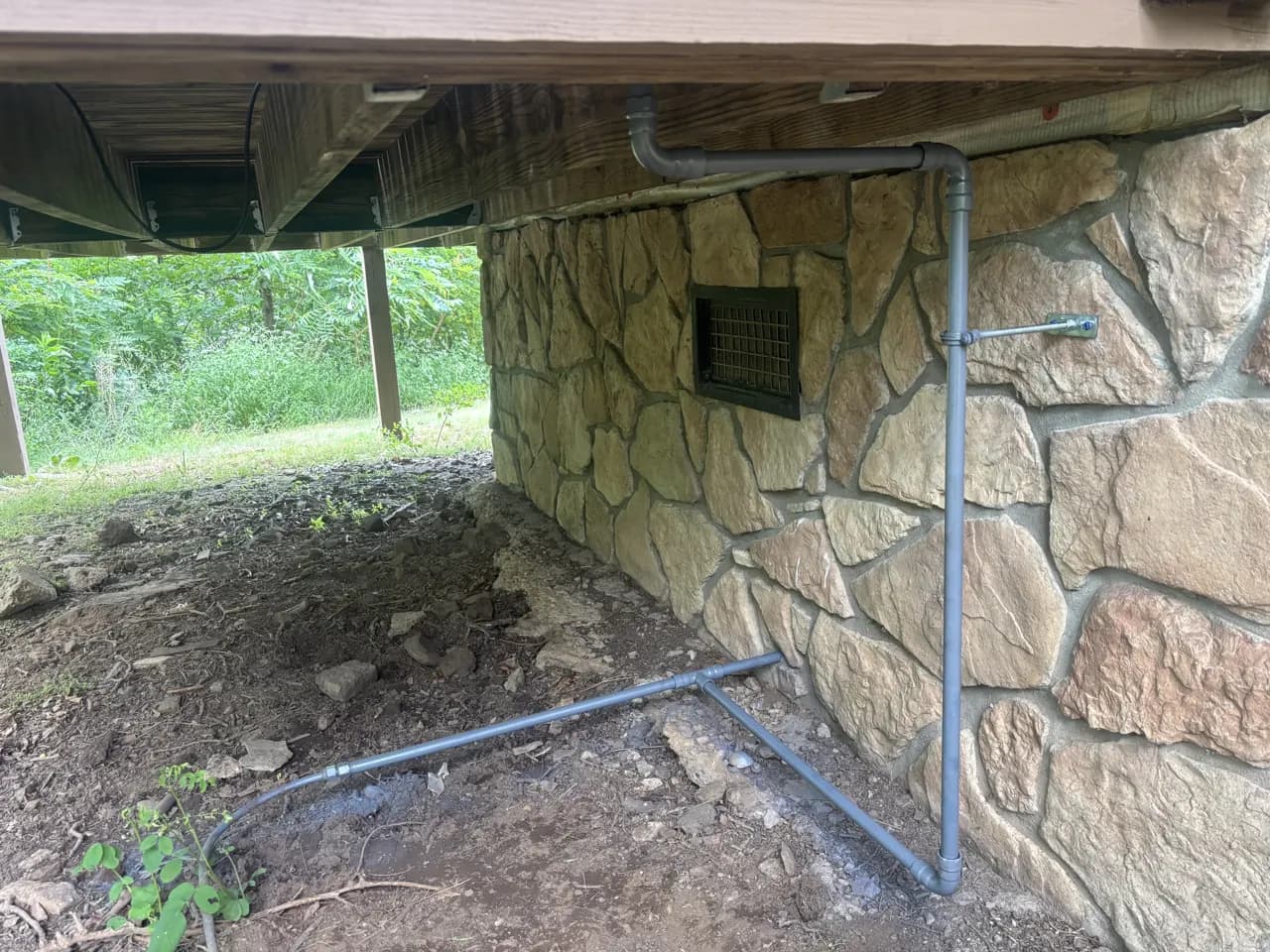 A new pipe run beneath a pier-and-beam home, strapped to the stone foundation