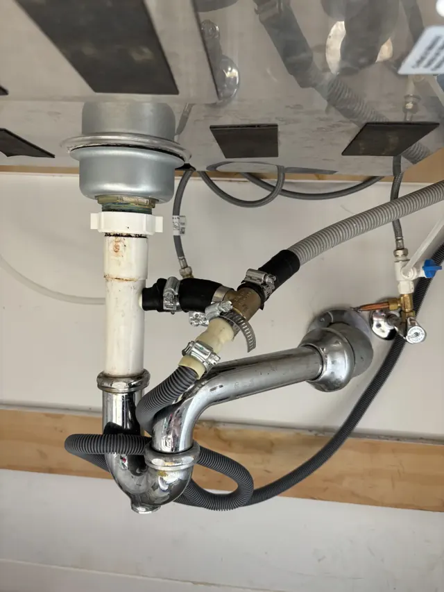 Kitchen sink drain before repair: mismatched fittings, clamps and a flexible hose patched together under the sink