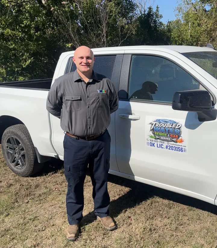 Dustin, owner of Troubled Water Sewer & Gas, standing beside his white work truck with the Troubled Water logo and OK LIC. #203156 on the door